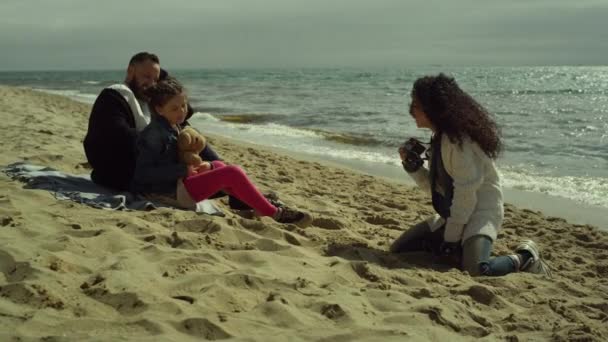 Doce família desfrutar de fotosessão na areia da praia. Pais criança posando imagem por mar. — Vídeo de Stock