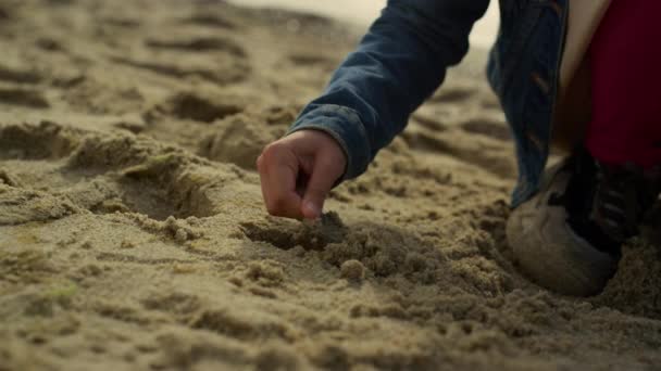 Счастливый ребенок играет в песок на океанском пляже. Улыбающийся ребенок веселится в одиночестве на берегу. — стоковое видео