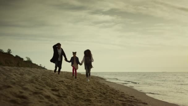 一家人在夕阳西下的海滨手牵手.妈妈爸爸的孩子放假在沙滩上跑来跑去. — 图库视频影像