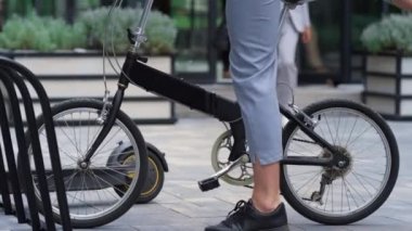 Şehir merkezinde kaldırımda bisikletten inen adam. Motorlu erkek bacakları yakın plan..