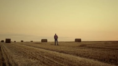Agrarian gün batımında samanlıkta yürüyor. Kırsal manzara kavramı