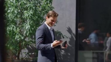 Gülümseyen finans işçisi modern iş yerinde akıllı telefonu kontrol ediyor..