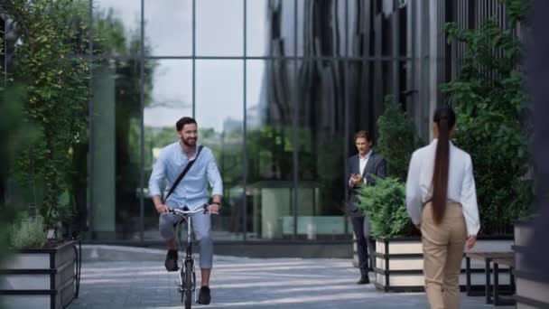 Un hombre de negocios sonriente montando bicicleta en un moderno edificio de oficinas. Joven empresario — Vídeos de Stock