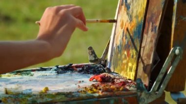 Ressam el dışarıda yağlı boya çiziyor. Bilinmeyen ressam tuvali yakından boyuyor