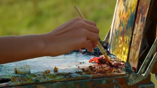 Unknown artist mixing paints on palette. Closeup hand drawing on canvas outdoors — Stock Video