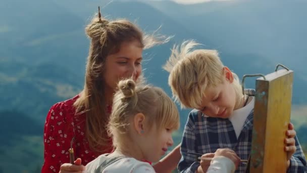 Familia sonriente creando imagen al aire libre. Niños pintando con madre en caballete. — Vídeo de stock