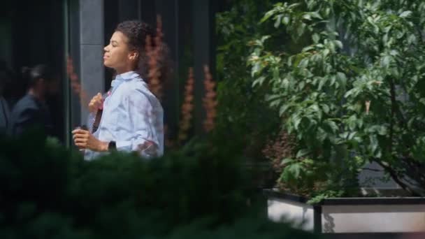 Mujer de negocios sonriente sosteniendo café taza caminando distrito de negocios en día soleado. — Vídeo de stock