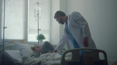 Doktor hastane koğuşundaki küçük hastayı kontrol ediyor. Hasta kız pelüş oyuncağı kucaklıyor