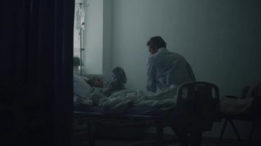 Doktor klinik koğuşundaki küçük hastayı ziyaret ediyor. Hasta kız yatakta pelüş oyuncağı kucaklıyor..