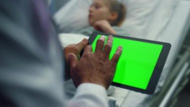 Doktor tablet yeşil ekrana dokunuyor. Hasta kız hastane yatağında yatıyor..