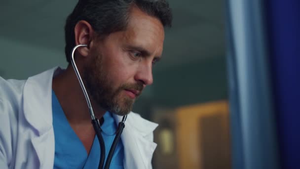 Vousatý terapeut poslouchající tlukot srdce neznámého pacienta na portrétu kliniky — Stock video