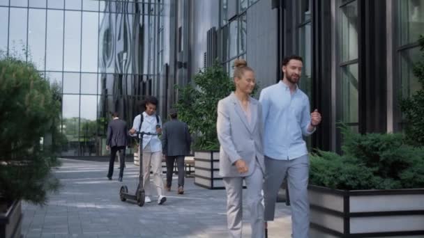 현대식 사무실 건물 근처에서 전기 스쿠터를 들고 걷는 미소짓는 관리인. — 비디오