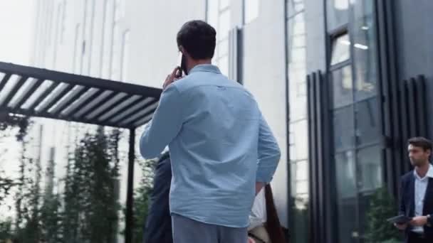 一个自信的男人在市中心讲电话.各个公司的人走路. — 图库视频影像