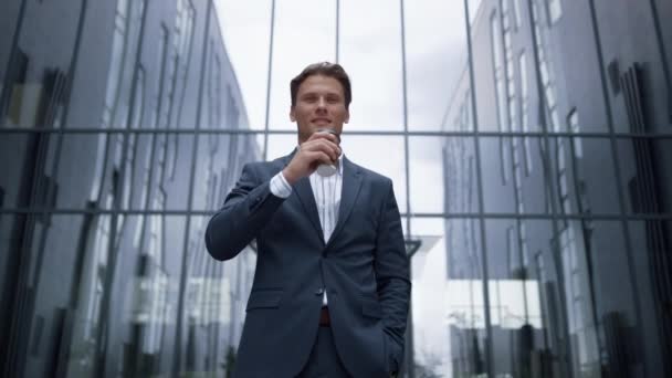 Retrato sorridente empresário beber café de pé no prédio de escritórios de vidro. — Vídeo de Stock
