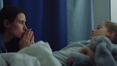 Üzgün kadın, küçük hasta kızı klinikte ziyaret ediyor. Çocuk hastane yatağında yatıyor..