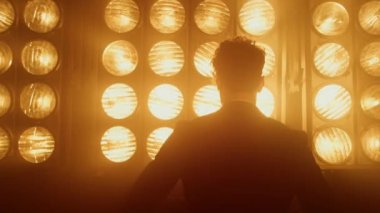 Gece kulübü ışıklarında dönen erkek model kapanıyor. Adam kendinden emin duruyor.