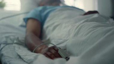 Hasta adam klinik koğuşunda oksijen maskesi soluyor. Nabız oksimetresi parmağa yakın çekim.