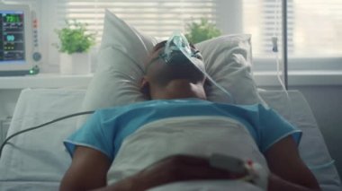 Yatakta yatan erkek hasta oksijen maskesi soluyor. Kapalı doktor elleri tablet kullanıyor