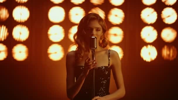 Горячая девушка вокалистка исполняет песню глядя камеру соблазнительно в студийных огнях. — стоковое видео