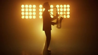 Siluet caz müzisyeni spot ışıklarında saksafon çalıyor. Melodi yapan adam.