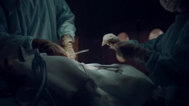 Cerrahlar tıbbi kıyafetin içinde dikiş kesiği atıyor. Karanlık ameliyathane kapalı..
