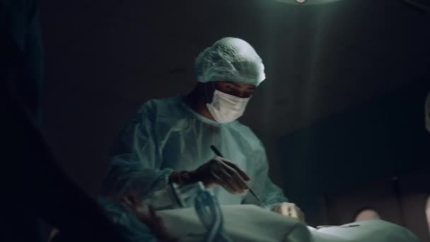 Chirurg opererend in een donkere spoedafdeling. Medische hulp die bloedige tampons neemt. — Stockvideo