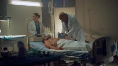 Doktor hastane koğuşunda defibrilatör kullanıyor. Klinik personeli hastanın hayatını kurtarıyor.