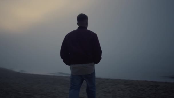 Giovane uomo che cammina sulla spiaggia sabbiosa nella nebbia mattutina. solitario ragazzo guardando mare orizzonte — Video Stock