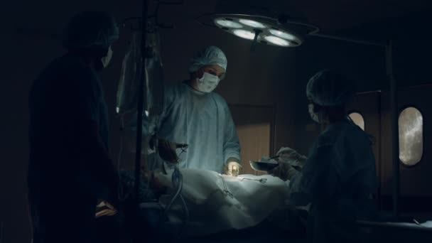 Впевнений хірург, який виконує операцію в темній стерильній клініці екстреної допомоги . — стокове відео