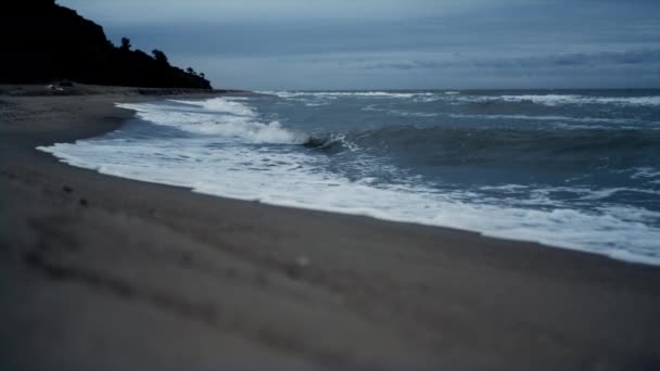 Havsvågor stänker sandstrand linje på kvällen havsutsikt. Mörkt vatten koncept — Stockvideo