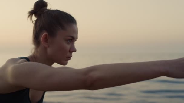 Fokuserad flicka som sträcker händerna framåt praktiserar yoga asana på havskusten. — Stockvideo