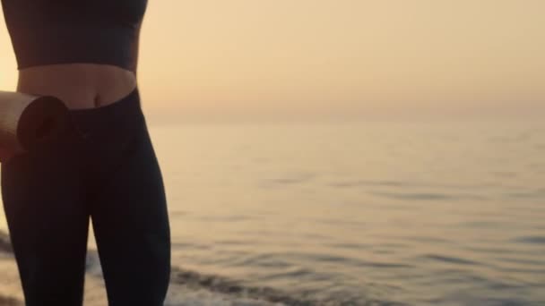 Pasująca dziewczyna trzymająca matę na brzegu o zachodzie słońca. Sportowiec idzie na trening. — Wideo stockowe