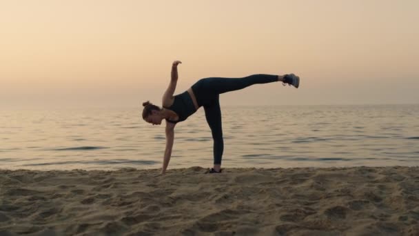 Дівчинка робить палючу шандрасану стоячим пляжем. Жінка практикує позу півмісяця . — стокове відео