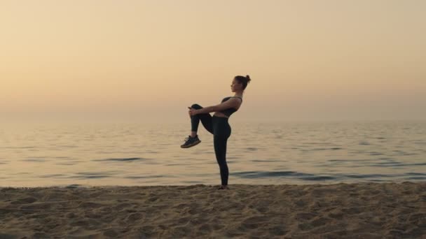 Sportowa dziewczyna trzymająca kolano rozprostowane nogi na plaży. Sportowiec rozgrzewa stopy. — Wideo stockowe