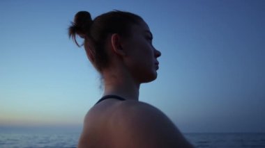 Profil kızı elini karanlık gökyüzüne kaldırıyor. Yaklaş. Kumsalda yoga yapan bir kadın..