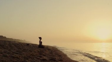 Sahilde meditasyon yapan odaklanmış bir kadın. Yoga yapan kadın lotus pozu veriyor..