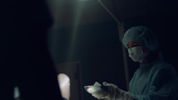 Enfermeira entregando instrumentos cirurgião segurando ferramentas estéreis na sala de emergência escura. — Vídeo de Stock