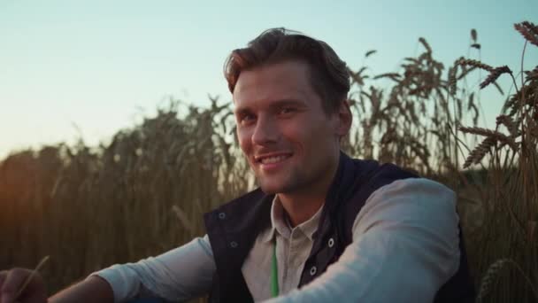 Uśmiechnięty rolnik pozujący na portrecie pola pszenicy. Zmęczony pracownik odpoczywający o zachodzie słońca. — Wideo stockowe