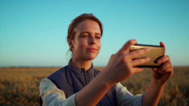 黄金の農地の眺めでフィールド写真を撮る女性。農業労働者の肖像. — ストック動画