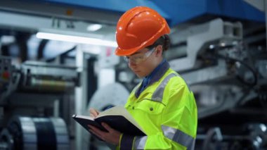 Endüstriyel üretim fabrikasındaki kameraya bakan denetçi işçi.