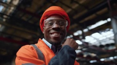 Büyük endüstriyel üretim deposundaki kameraya bakan neşeli bir yönetici.