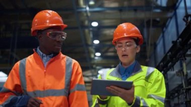 Ortaklar tablet bilgisayarı tutarken devasa modern üretim deposunda yürüyorlar..