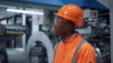 Afro-Amerikan mühendis modern endüstriyel üretim fabrikasında kamera arıyor.