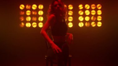 Kız erotik hareketler yapıyor. Gece kulübü sahnesinde oturuyor. Yakın çekim.