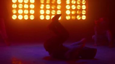 Güçlü adam yel değirmenini icra ediyor. Dansçı numaralar gösteriyor.