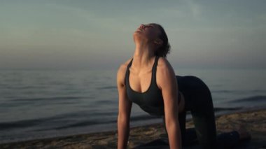 Kedi ineği pozu veren sporcu kadın kumlu sahilde yoga yapıyor. Yakın çekim.. 