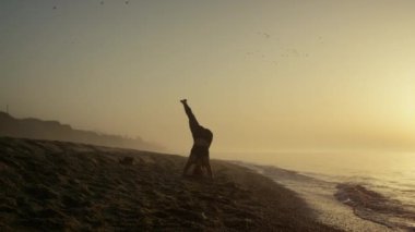 Siluet kız başının üstünde duruyor. Yogacı kadın gün doğumunda antrenman yapıyor..
