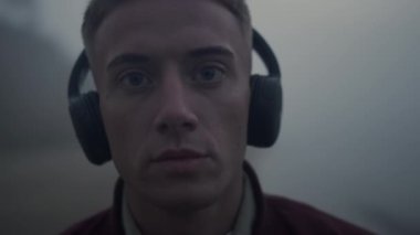 Kulaklıkla müzik dinleyen yakışıklı adam. Kameraya poz veren yakın plan odaklı adam.