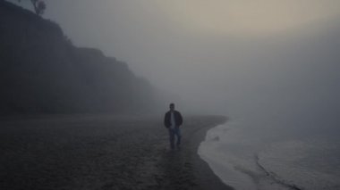 Sisli gündoğumunda kumsalda yürüyen yalnız bir adam. İnsan sislerin içinde doğayı keşfediyor