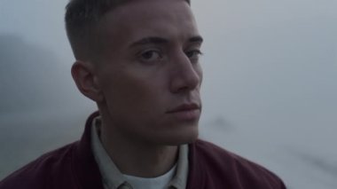 Deniz kıyısındaki portrede kameraya poz veren üzgün adam. Yakın plan üzgün adam başka tarafa bakıyor.